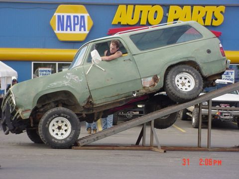 1976 Jeep CJ7 - A green SUV with significant rust damage is positioned on a ramp in front of a NAPA Auto Parts store, with another vehicle visible in the b…
