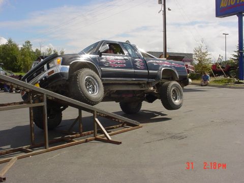 1976 Jeep CJ7 - A modified black pickup truck is partially on a metal ramp with its rear wheels in the air.