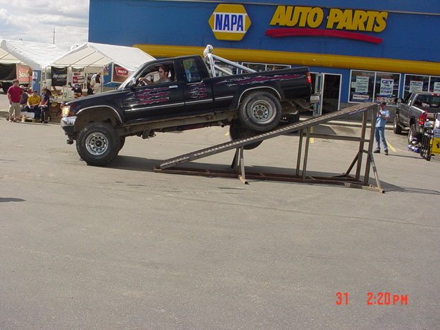 Black pickup truck with custom graphics on a ramp in front of a NAPA Auto Parts store