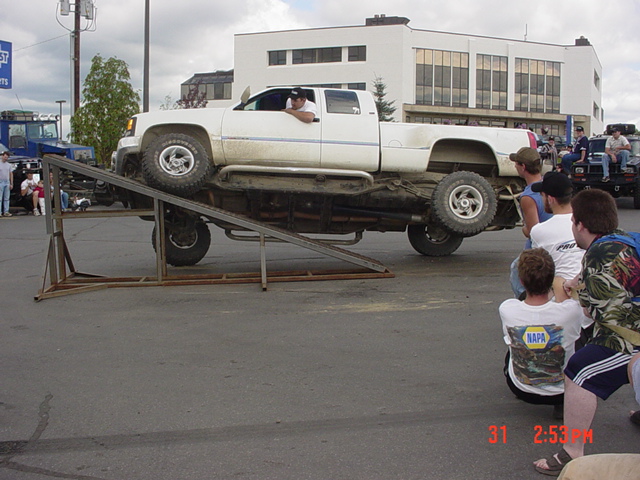 White lifted GM pickup climbing a steel teeter-totter ramp at an outdoor event
