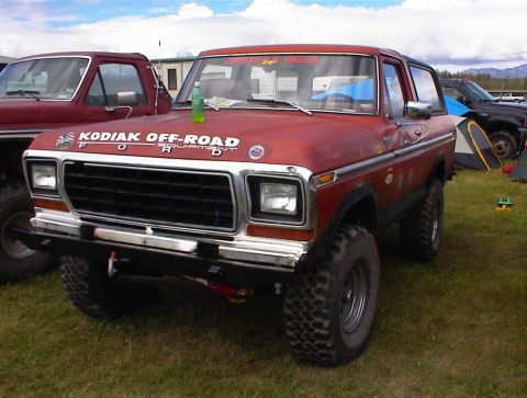 1978 Ford Bronco - A red 1978 Ford Bronco is parked on grass with other vehicles and tents in the background.