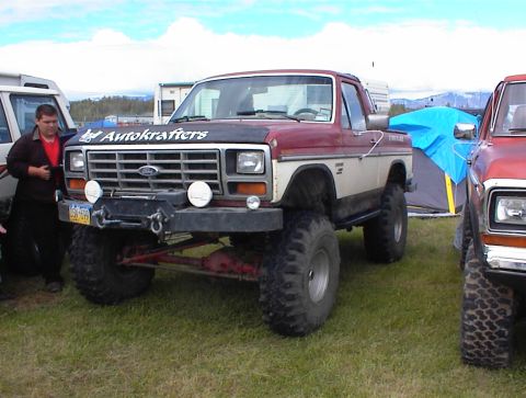 1978 Ford Bronco - A lifted 1978 Ford pickup truck with a two-tone paint scheme and off-road tires is parked on grass next to another vehicle.