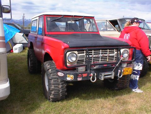 1978 Ford Bronco - A red 1978 Ford Bronco with a white roof and a winch is parked outdoors, with other vehicles and tents nearby.