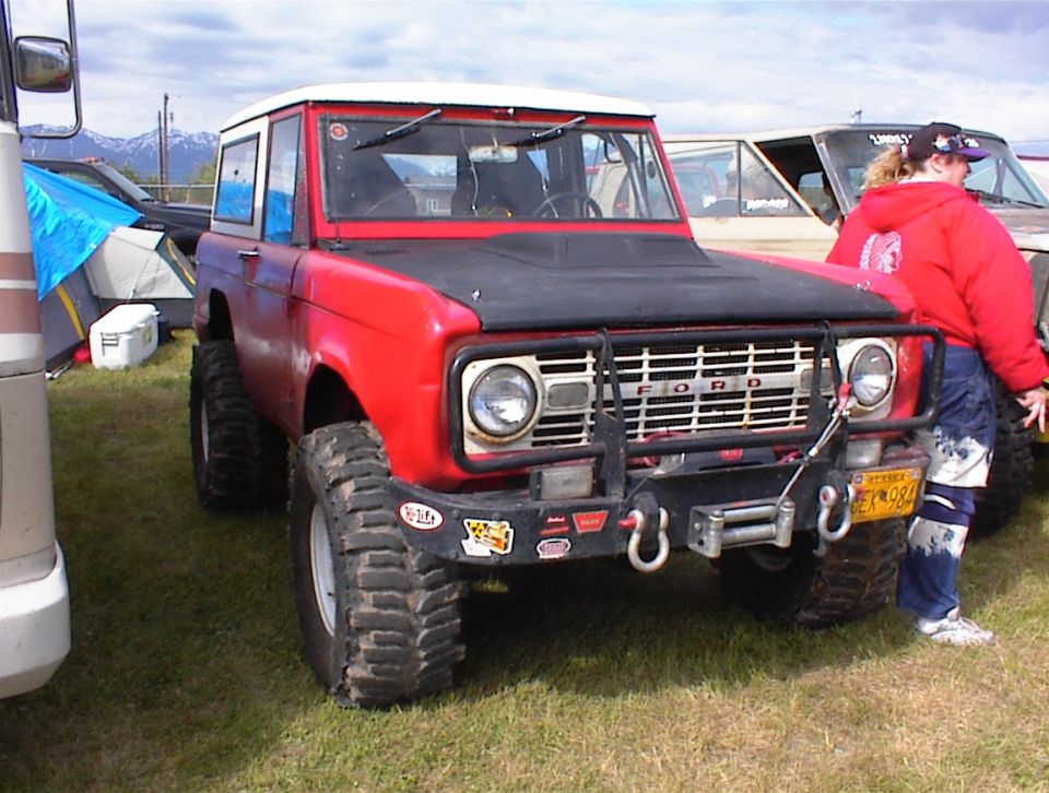 Red 1978 Ford Bronco with a winch and off-road tires, parked on grass