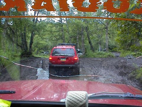 1978 Ford Bronco - Two vehicles navigate a challenging muddy trail through a dense forest.