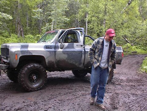 1978 Ford Bronco - Camouflaged pickup truck on a muddy trail with a man standing nearby. The truck's grille suggests a 1975 model year.