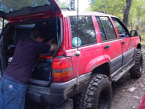 1978 Ford Bronco - A person loads gear into the back of a red Jeep Grand Cherokee modified for off-road use.
