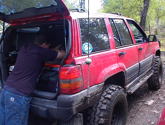 Red Jeep Grand Cherokee with large off-road tires, rear hatch open, person loading gear