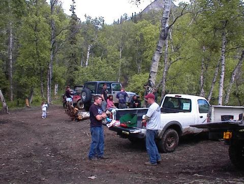 1978 Ford Bronco - Several vehicles and people are gathered in a wooded area, possibly for an outdoor event.