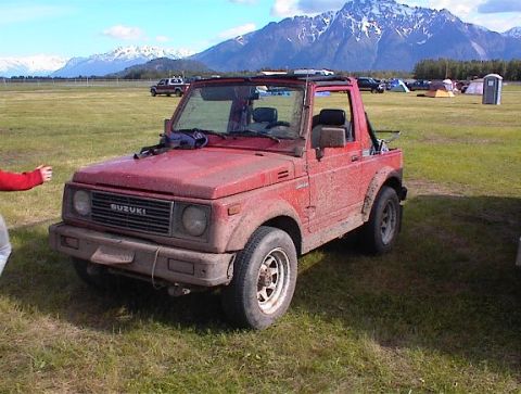 1978 Ford Bronco - Suzuki Samurai with mountains and tents in the background.