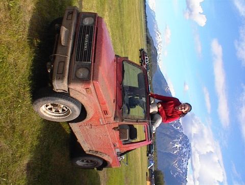 1978 Ford Bronco - A person poses in the doorway of a red Suzuki Samurai with a mountain range behind it.