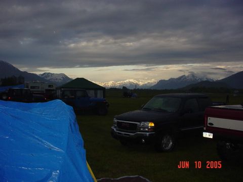 1978 Ford Bronco - A campsite scene with multiple vehicles and tents under a cloudy sky with snow-capped mountains.