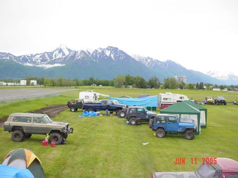 1978 Ford Bronco - Several off-road vehicles and campers are gathered on a field with a mountain range in the distance.