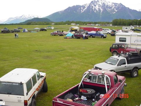 1978 Ford Bronco - A gathering of trucks, SUVs, and RVs in a field with a mountain range behind them.