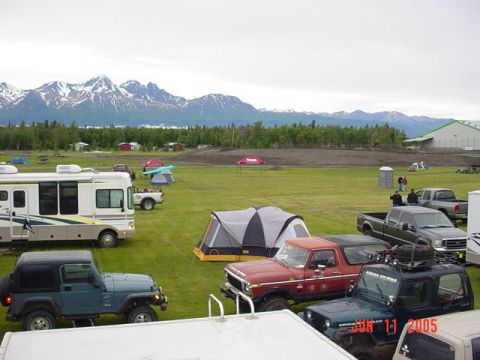 1978 Ford Bronco - A campsite scene with multiple vehicles and tents, set against a backdrop of mountains and a large building.