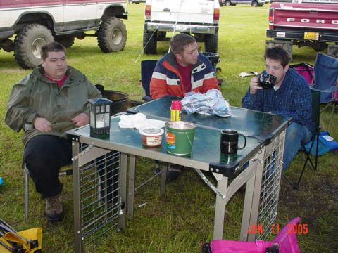 1978 Ford Bronco - Three men are gathered around a table outdoors, with several large trucks parked behind them.