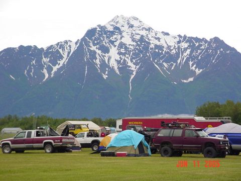 1978 Ford Bronco - Several vehicles and tents are set up in a field with a large mountain range in the background.