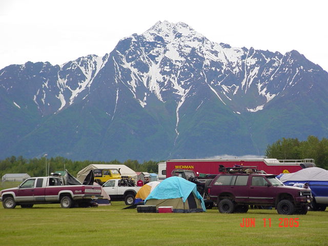 Maroon SUV parked on grass with a blue tarp covering another vehicle behind it