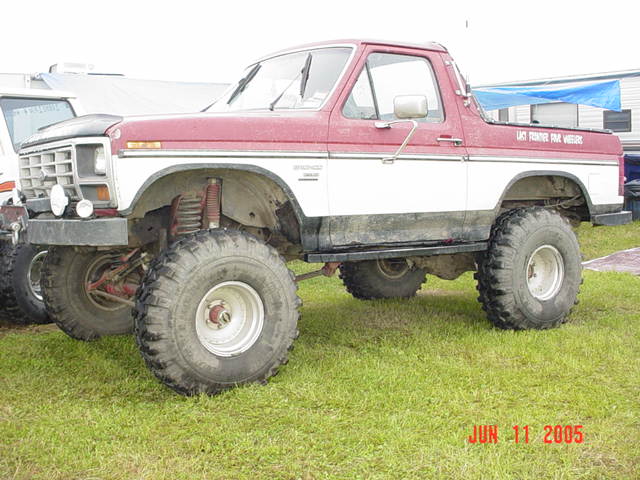 Side view of a red and white 1978 Ford Bronco lifted with large off-road tires