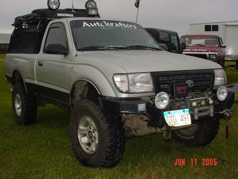 1978 Ford Bronco - A modified Toyota Tacoma is parked on grass with other vehicles in the background.
