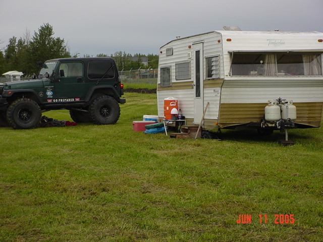 Green Jeep Wrangler parked next to a white and gold travel trailer on a grassy field. Date stamp reads JUN 11 2005