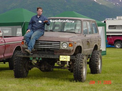 1978 Ford Bronco - Man poses on a heavily modified SUV at an outdoor event. The vehicle has oversized tires and custom decals.