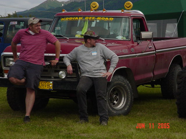 Two guys leaning on a red pickup truck. Truck has 'KODIAK OFF-ROAD' on windshield and smiley face lights on roof