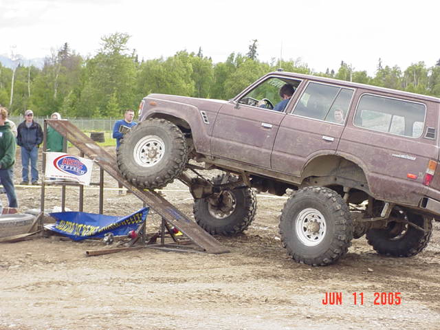 Brown off-road SUV with large tires climbing a metal ramp, driver visible