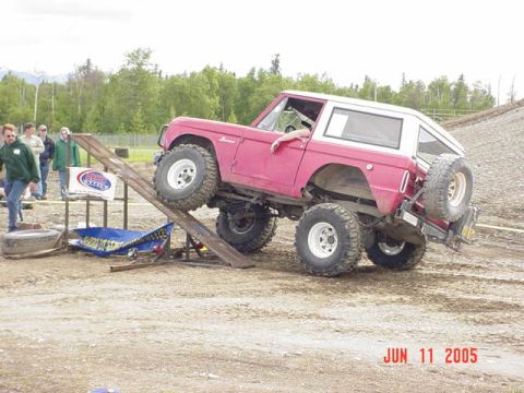 1978 Ford Bronco - A red and white 1978 Ford Bronco navigates an obstacle course, climbing a wooden ramp with its front wheels elevated.