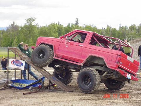 1978 Ford Bronco - A red 1980s Ford Bronco with a roll cage is on a ramp during an off-road event.