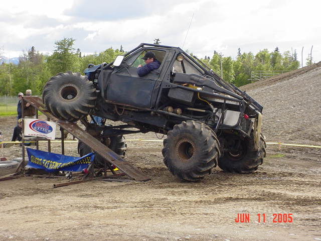 Black custom off-road truck with large tires on a ramp, driver visible