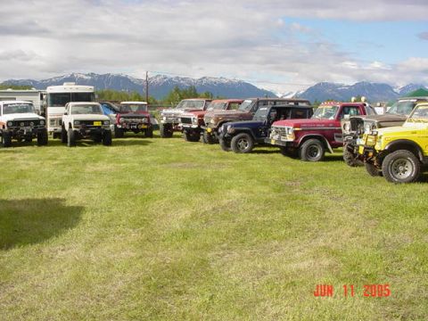 1978 Ford Bronco - A group of off-road vehicles gathered on a grassy field, with snow-capped mountains in the distance.