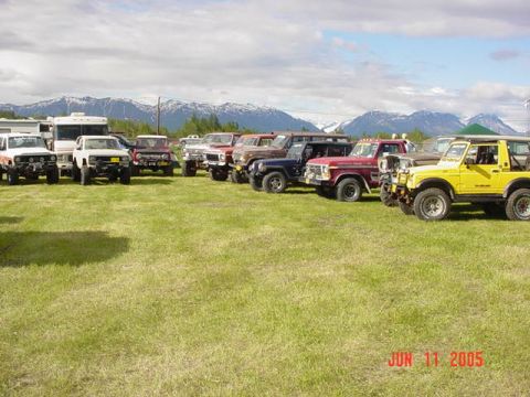 1978 Ford Bronco - A group of off-road vehicles are gathered in a grassy field with mountains in the distance.