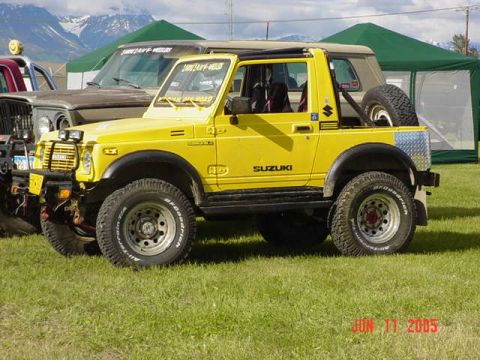 1978 Ford Bronco - A yellow Suzuki Samurai is parked on a grassy field with tents and mountains in the background.