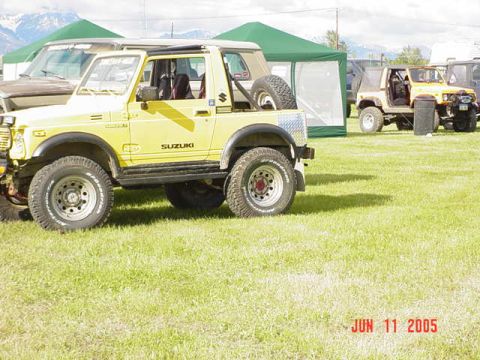 1978 Ford Bronco - A yellow Suzuki Samurai is parked on a grassy field next to other vehicles and tents.