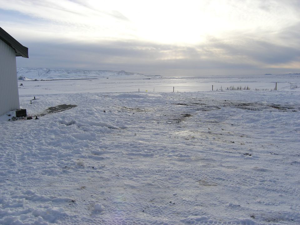 Snowy landscape with a building on the left and mountains in the distance under a cloudy sky