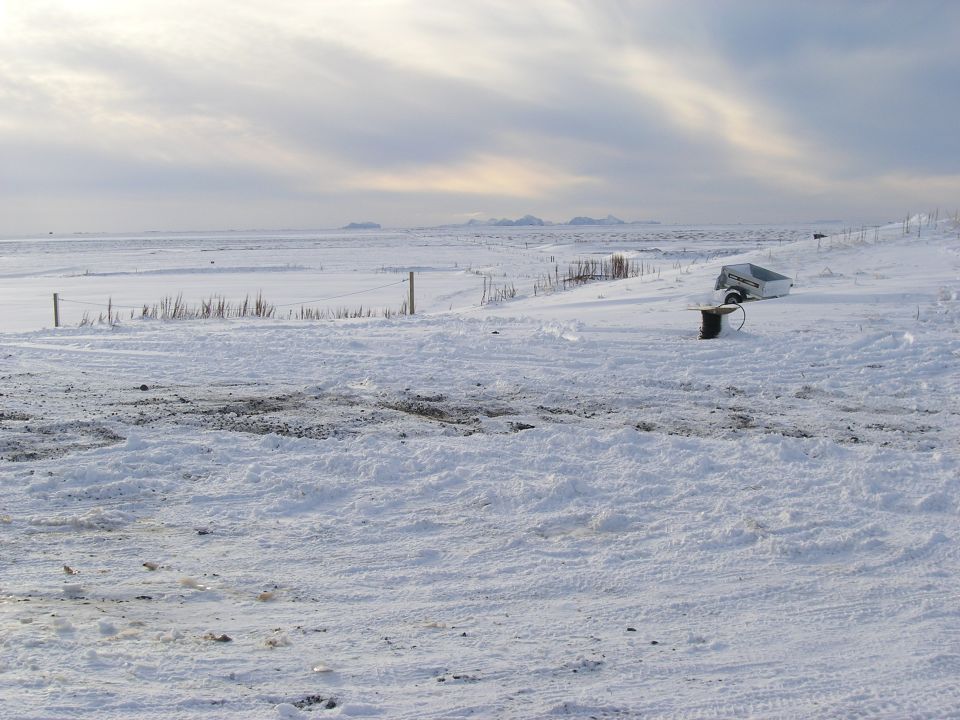 trailer sitting in a snowy field with a wire spool next to it