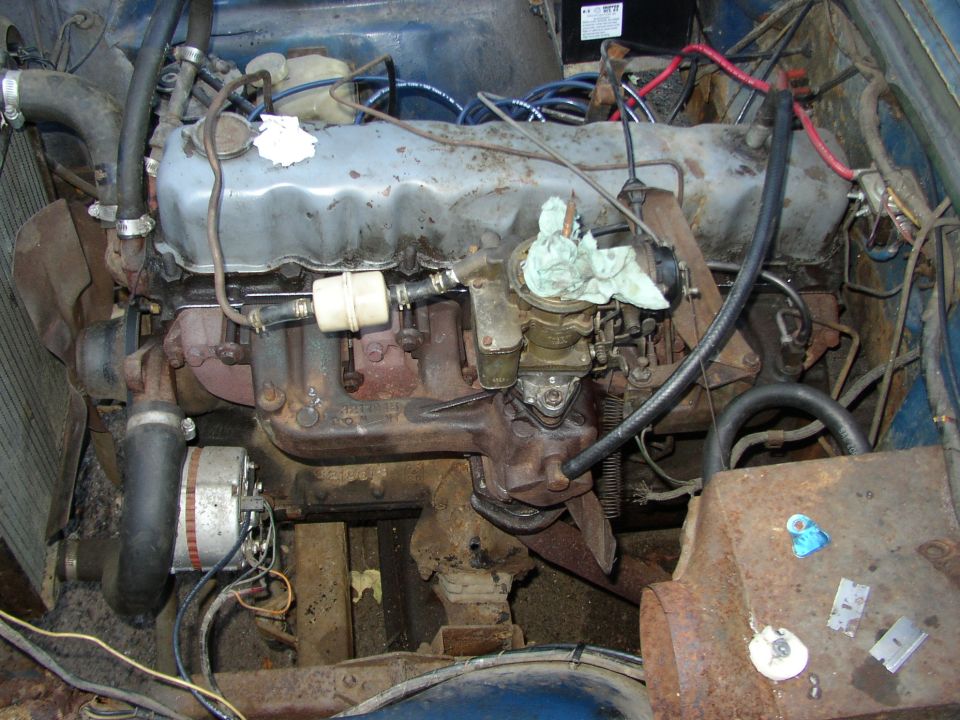 Engine bay with a blue vehicle's engine, carburetor, and alternator visible