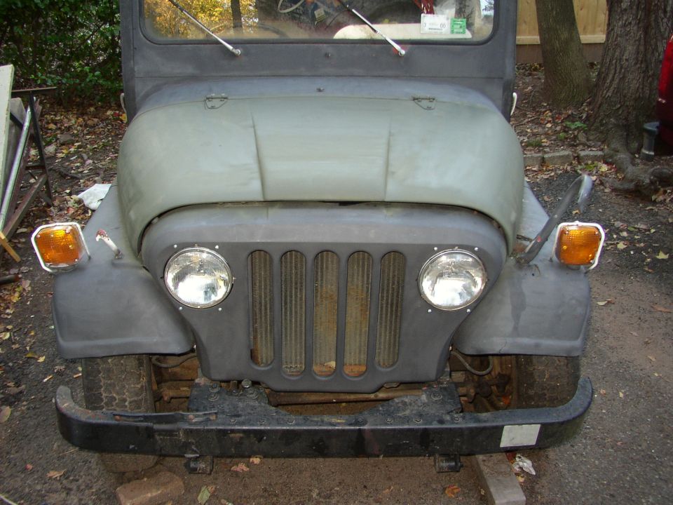 Front view of a Jeep CJ with round headlights and vertical grille slots. Orange turn signals are mounted on the fenders