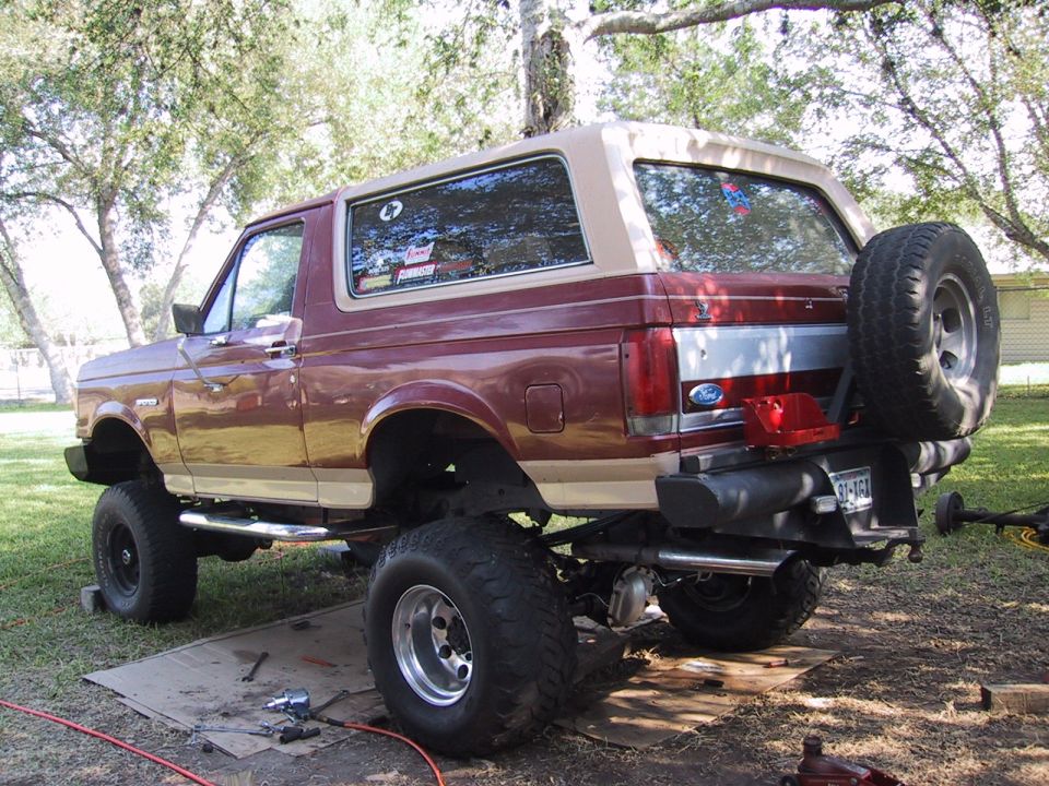 Maroon and tan lifted Ford Bronco SUV, rear 3/4 view, outdoors on plywood