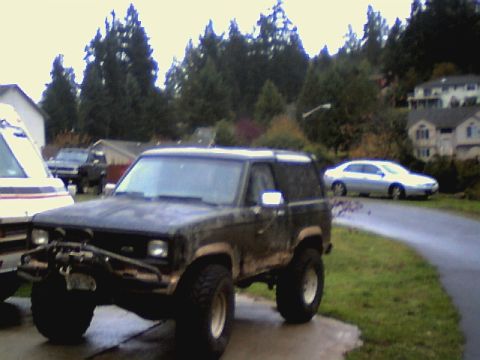 1987 Ford Bronco II - A lifted 1987 Ford Bronco II sits parked on a wet driveway, ready for off-road adventures.