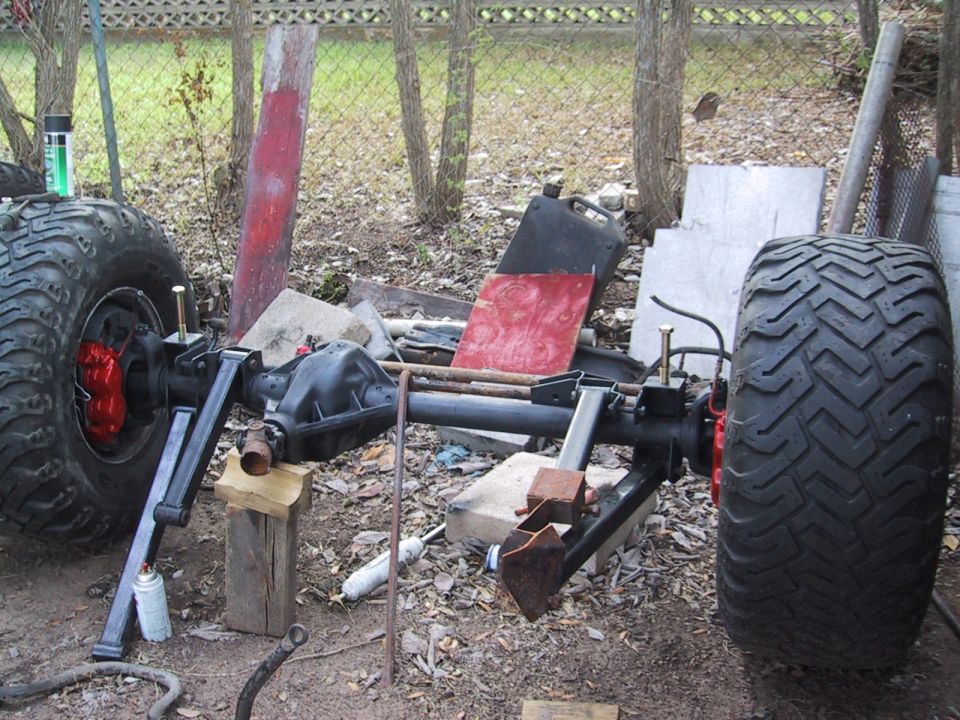 Two large off-road tires and axles are visible, supported by wooden blocks and metal brackets