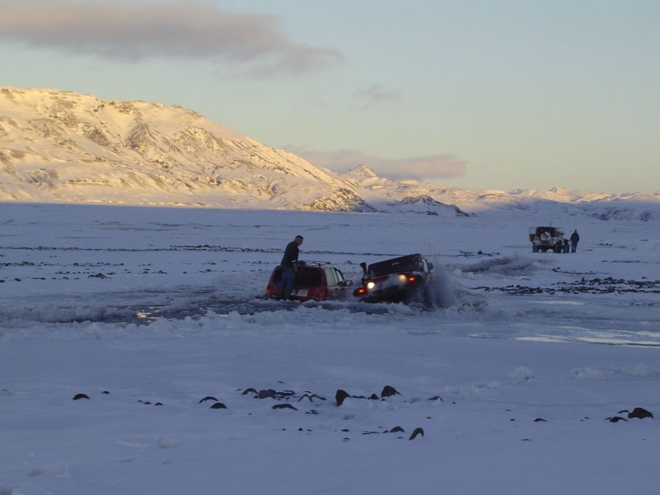 Two Jeep Wranglers driving through icy water with a snowy mountain range in the background