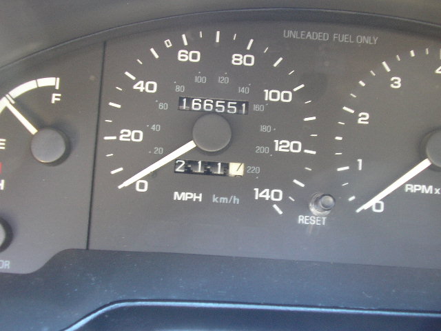 Car dashboard with speedometer, fuel gauge, and odometer showing 166551 miles