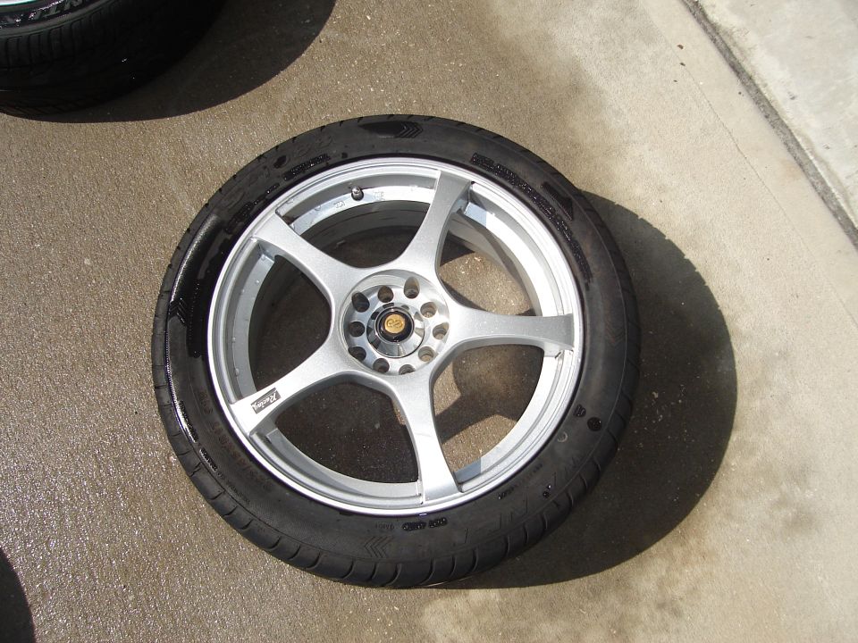 Silver 5-spoke wheel with tire on concrete. Text on wheel reads 'Racing'