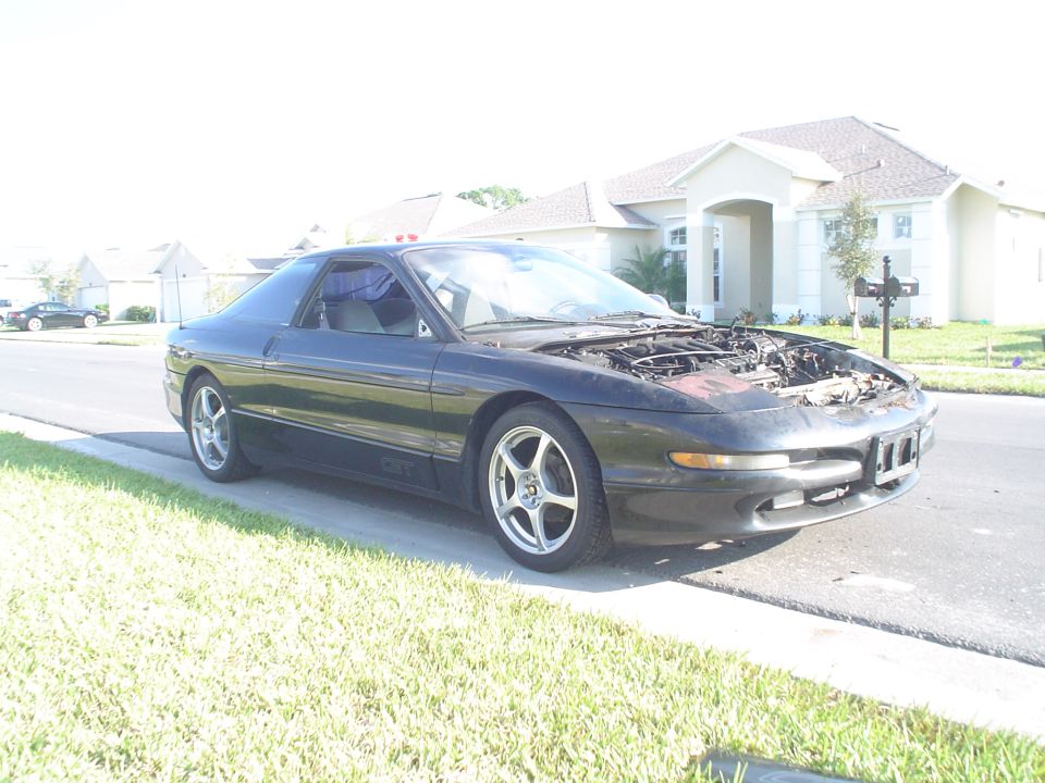 Black 1994 Ford Probe coupe parked on a residential street with hood open, showing the engine bay