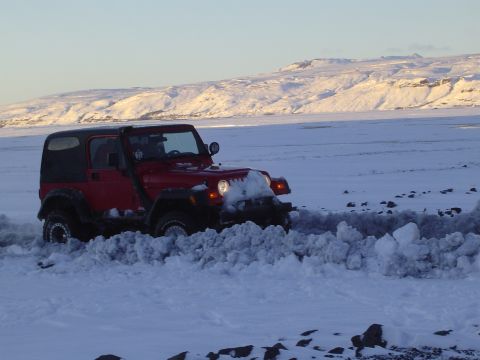 2001 Jeep Wrangler - A red Jeep Wrangler navigates a snowy landscape, pushing snow aside as it moves forward.