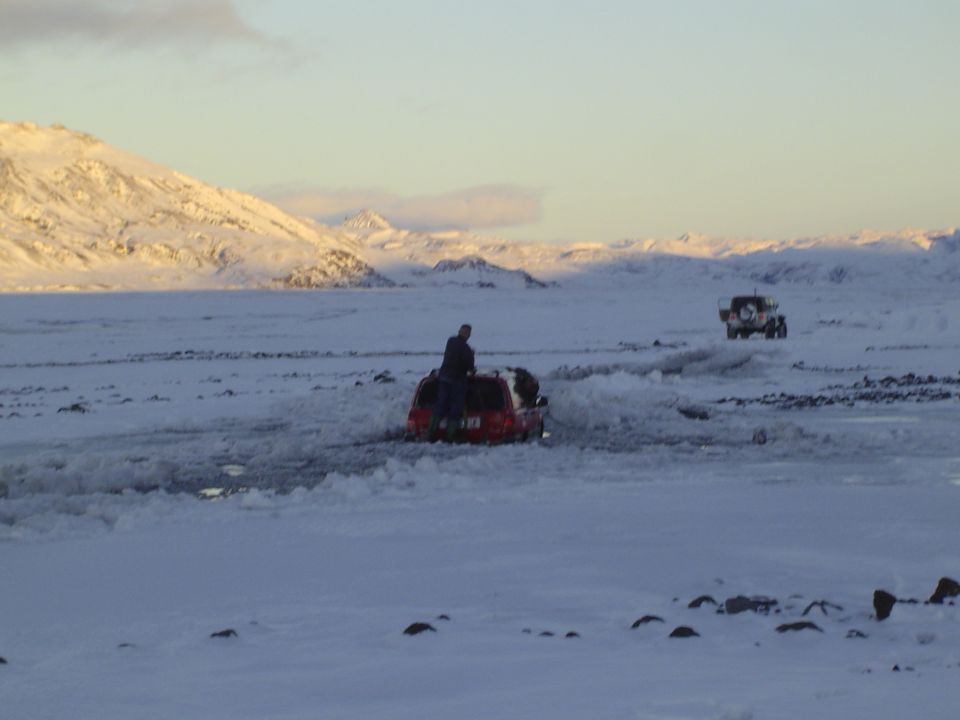 Two SUVs driving through snow-covered terrain with mountains in the background