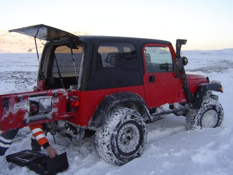 2001 Jeep Wrangler - A red 2001 Jeep TJ equipped with a snorkel is stuck in the snow, with its rear door open and someone working on a toolbox.