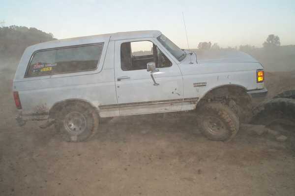 Dusty white Ford Bronco on mud tires climbing a dirt mound at an off-road park
